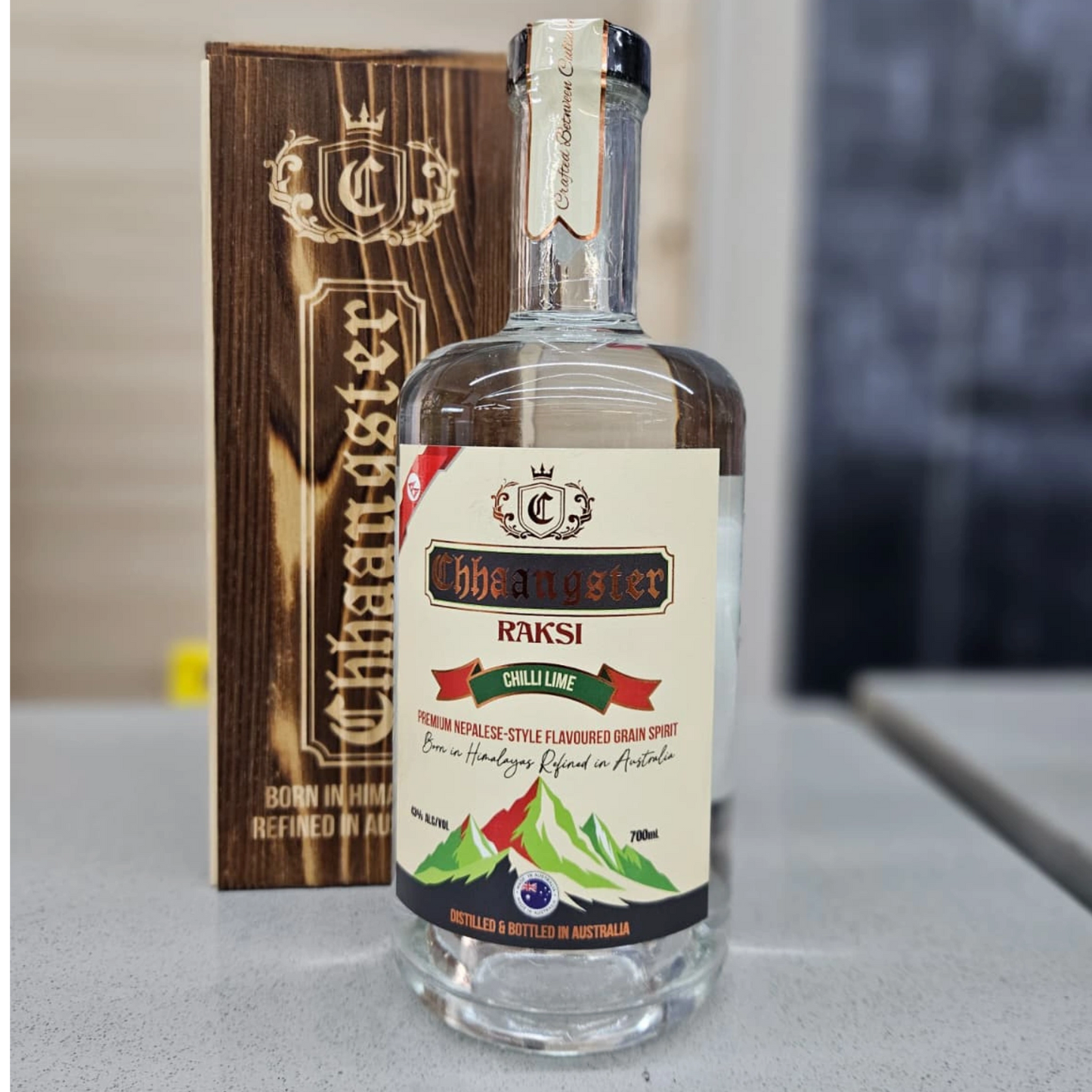 Bottle of Chhaangster RAKSI Chilli Lime flavored grain spirit with a wooden box in the background.